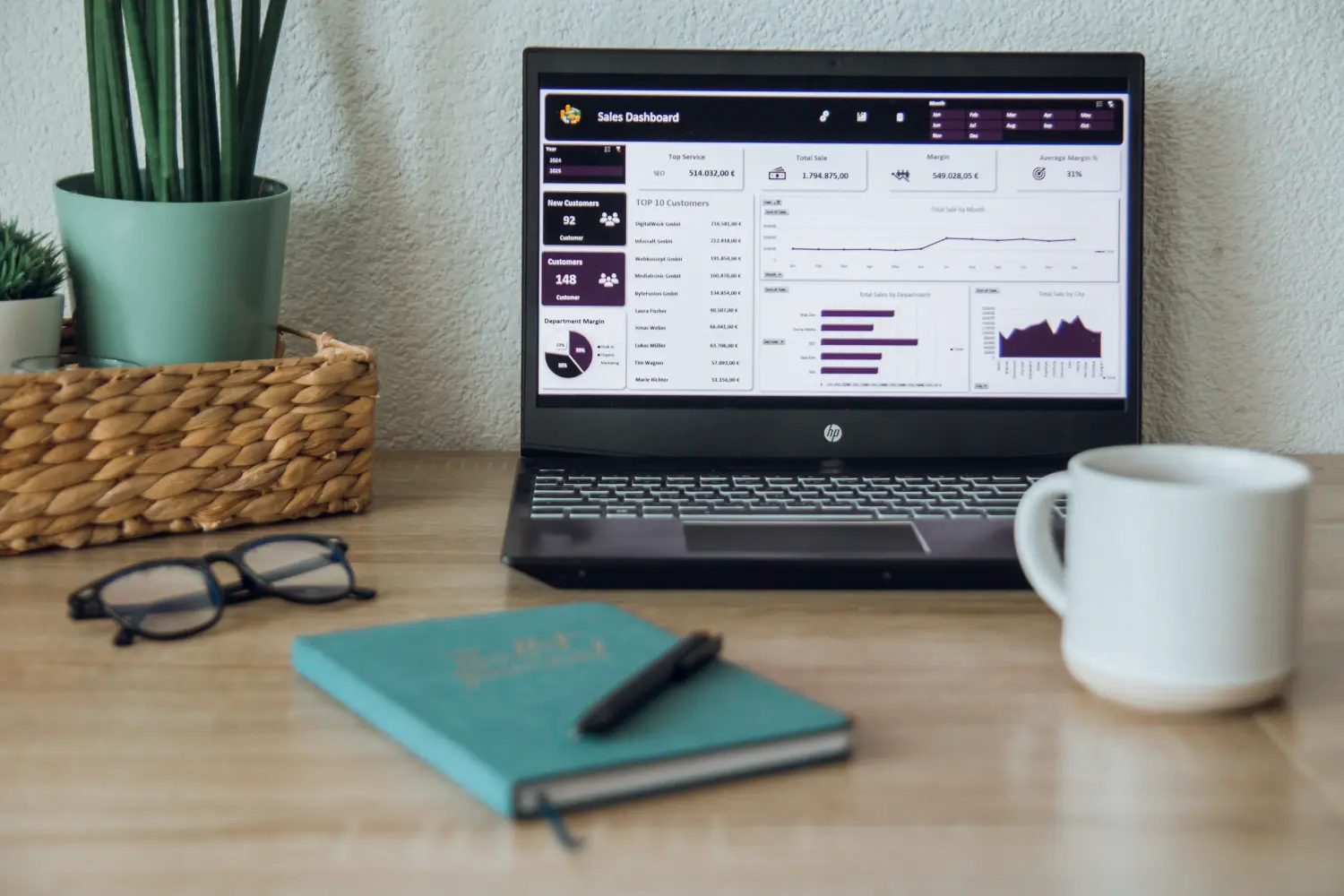 Ein Laptop mit einem Dashboard für Personalmanagement oder Business Intelligence sowie ein offener Planer oder ein Notizbuch mit Schreibutensilien suggerieren eine Arbeits- oder Lernumgebung.