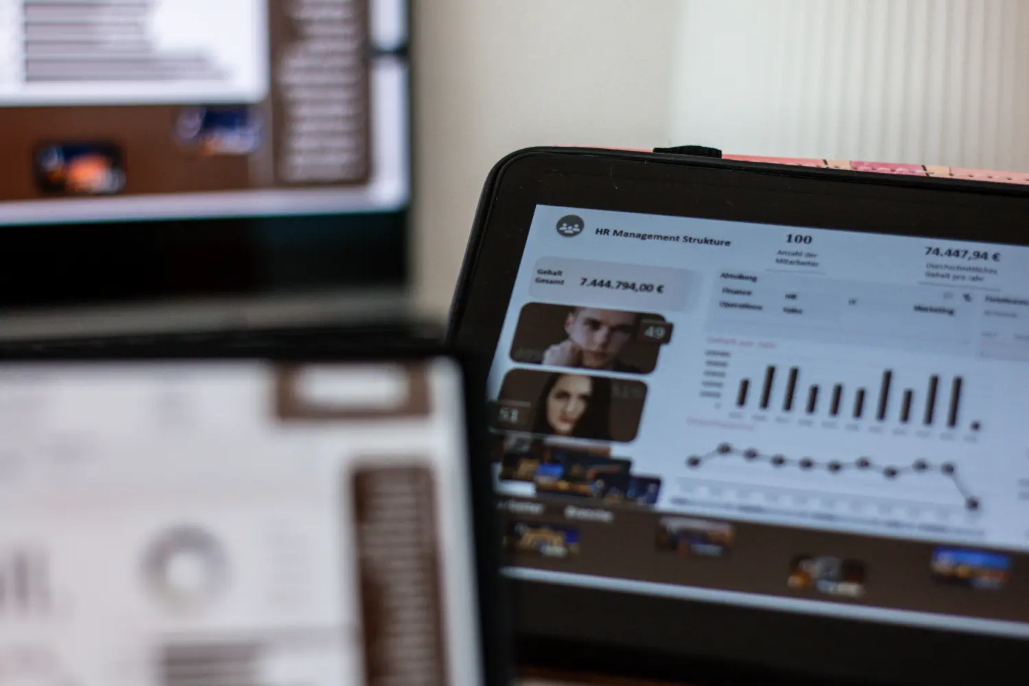 Ein Laptop mit einem Dashboard, das an ein Personalmanagement- oder Business-Intelligence-Dashboard erinnert, sowie ein offener Planer oder ein Notizbuch und Schreibutensilien suggerieren eine Arbeits- oder Lernumgebung.